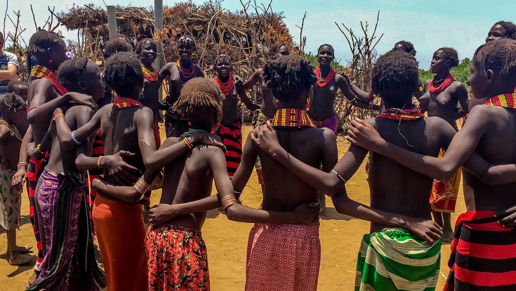 Hamar women and men in beaded jewellery and bright cloth, standing in a circle at a village gathering in the Omo Valley.