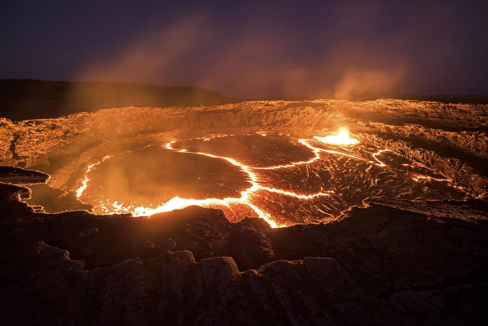 The lava lake of the Erta Ale volcano glowing orange across a dark crater floor at night.